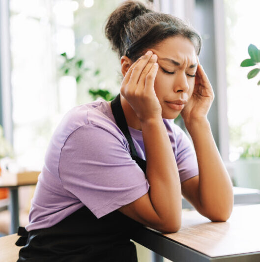 Young waitress suffering from headache while working in cafe Chronic and Autoimmune Conditions Migraines