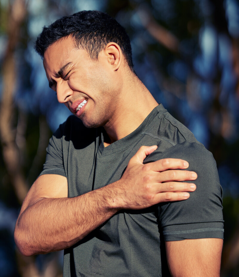 Shot of a sporty young man holding his shoulder in pain while exercising outdoors.
